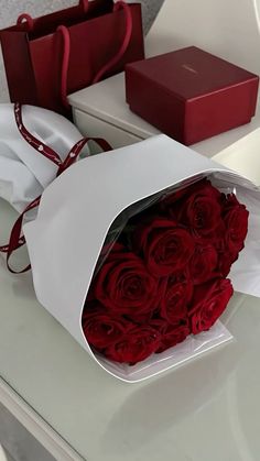 a bouquet of red roses in a white paper bag on a table next to some boxes