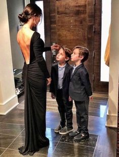 a woman in a black dress standing next to two boys