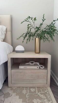 a nightstand with a plant on top of it next to a bed