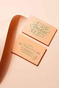 two business cards sitting next to each other on top of a white surface with green lettering