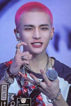 a man with pink hair and piercings holding a microphone in front of a screen