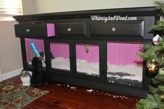 a black dresser with pink and white paint on the side, next to a christmas tree