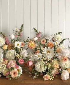 three vases filled with flowers on top of a wooden table in front of a white wall