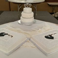 a white wedding cake sitting on top of a table next to two napkins that are shaped like hearts