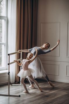 two young ballerinas are practicing their moves in the dance studio, one is holding on to the bars