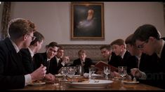 a group of young men sitting around a table eating food and drinking wine in front of them