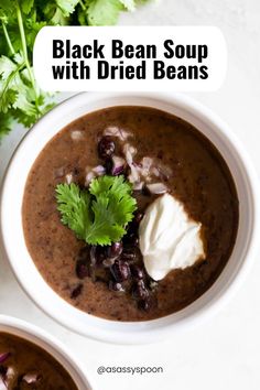 two bowls of black bean soup with dried beans and sour cream on the top one bowl is white