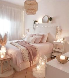 a bedroom with white walls and pink bedding, candles on the nightstands and lights hanging from the ceiling