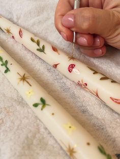 two white candles with designs on them being held by someone's hand