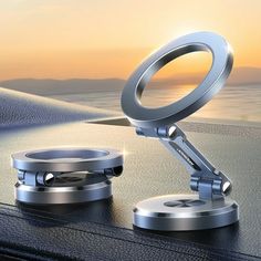 two rings on top of a table next to the ocean at sunset, with one being held up by a scissor