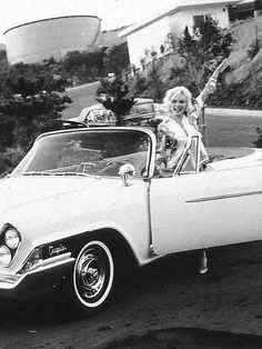 a woman is sitting in the driver's seat of an old car and waving