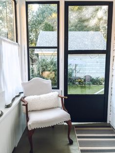 a white chair sitting in front of a window next to a black and white striped rug