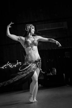 a belly dancer is dancing in the dark with her arms spread out and headbands down