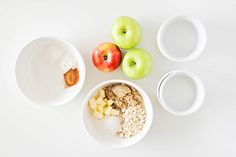 apples, oatmeal, and other ingredients in bowls on a white surface