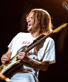 a man with long hair holding a guitar in his hand and singing into a microphone