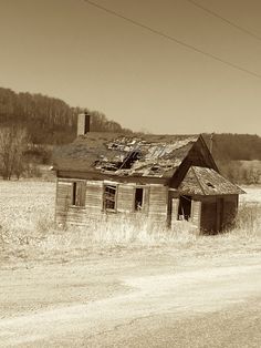 an old run down house sitting on the side of a dirt road next to a field