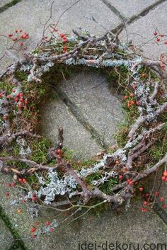 a wreath made out of branches and berries on the ground with moss growing around it