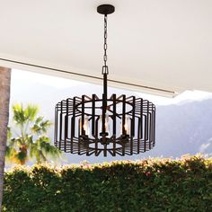 a chandelier hanging from the ceiling in front of some bushes and palm trees