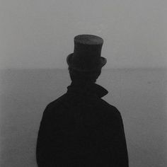 a black and white photo of a man with a top hat on his head standing in the fog