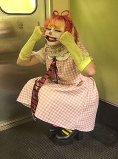 a woman with red hair and makeup is sitting on a subway train while holding her hands up to her face