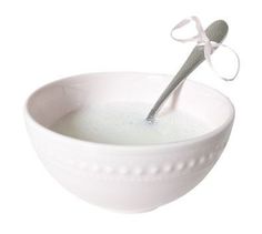 a white bowl filled with liquid and a spoon sticking out of the top, on a white background