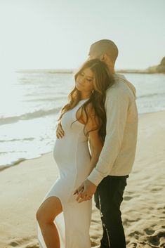 a pregnant woman standing next to a man on the beach