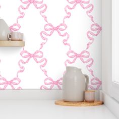 a white vase sitting on top of a counter next to a wall with pink bows