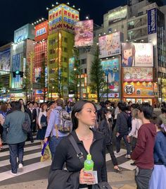 a woman standing in the middle of a cross walk at night with lots of people