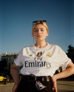 a woman with sunglasses on her head standing in front of a building wearing a white shirt and black pants