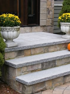 an orange pumpkin sitting on the steps of a stone house with two planters full of yellow flowers