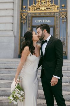 a newly married couple kissing in front of the city hall