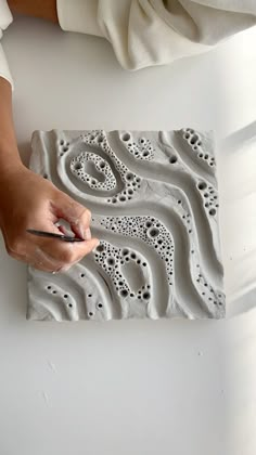 a person is using a pen to draw something on a piece of clay that looks like waves