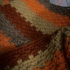 an orange and grey crocheted blanket laying on top of a bed