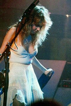 a woman with long hair standing in front of a microphone and wearing a white dress