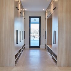 an empty hallway with wooden cabinets and black glass doors leading to the front door is lit by recessed lights