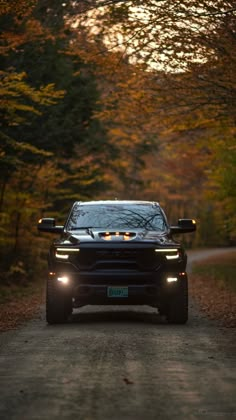 the front end of a black car driving down a dirt road with trees in the background