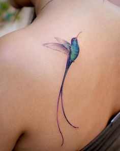 the back of a woman's shoulder with a hummingbird tattoo design on it