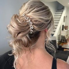 a woman with blonde hair in a messy updo wearing a white top and pearls on her head