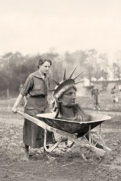 an old black and white photo of a woman pushing a wheelbarrow with the statue of liberty on it