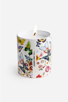 a white candle with colorful butterflies and flowers on the inside, sitting in front of a white background