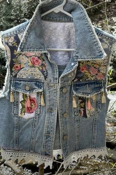 an old jean jacket with flowers and tassels hanging on a clothes rack in the woods