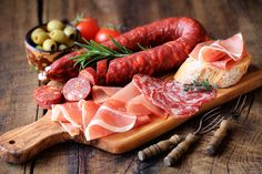 some meats are on a cutting board with olives, tomatoes, and bread