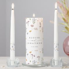 three white candles sitting next to each other on top of a table with pink flowers