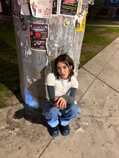 a young woman sitting on the sidewalk next to a pole