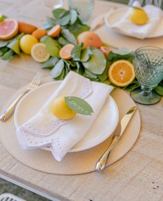 the table is set with plates, silverware and citrus fruit on it's edges