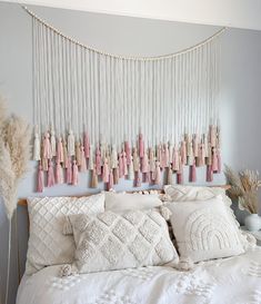 a white bed topped with lots of pillows next to a wall mounted art piece on the wall