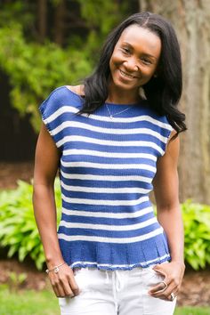 a woman standing in the grass wearing a blue and white striped top