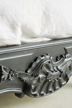 an ornate bed frame with white linens in the background and a pillow on top