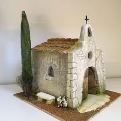 a small house made out of clay with a cross on the roof and trees in front