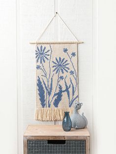 a blue vase sitting on top of a wooden cabinet next to a wall hanging with flowers